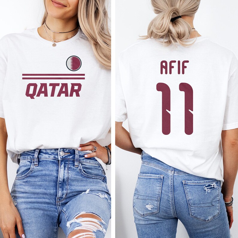 A woman wearing a white t-shirt with the word "Qatar" printed on it, and a number "11" on the back. She is also wearing distressed jeans.