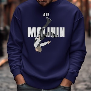May include: Navy blue sweatshirt featuring a graphic of a figure skater mid-air, with the word "AIR" above and "MALININ" in bold white letters. The skater is wearing a black and white outfit. The sweatshirt is a solid color.