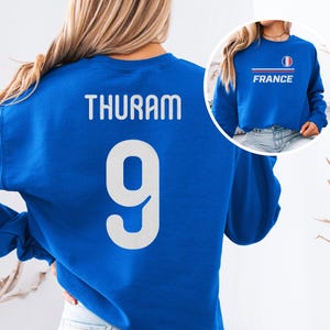 A woman wearing a blue sweatshirt with the number 9 and the name "Thuam" printed on it.