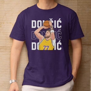 May include: Purple t-shirt featuring a basketball player in a yellow jersey with the number 77, mid-shot. The name "DONČIĆ" is printed vertically in white. The player is holding a basketball, ready to shoot.