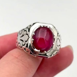 Puede incluir: Un anillo de plata con un diseño adornado y una gran piedra redonda de color rojo.