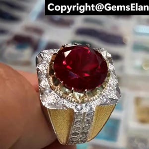 May include: An elaborate ring with a large, faceted red gemstone. The ring has a gold band and is detailed with silver and small, clear stones. The text "Copyright@GemsElan" is visible at the top.