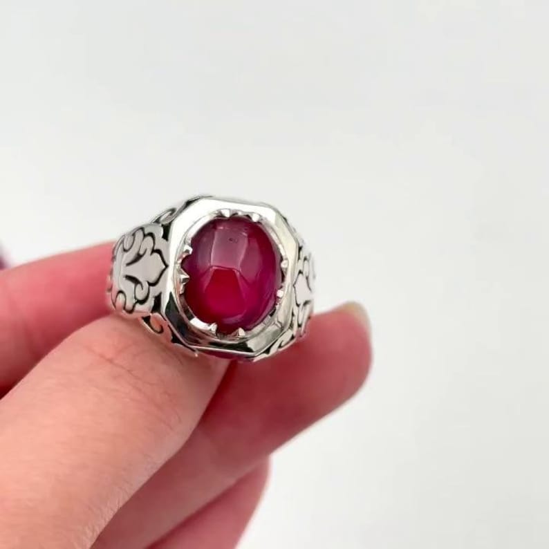May include: A silver ring with an ornate design and a large, round, red gemstone.