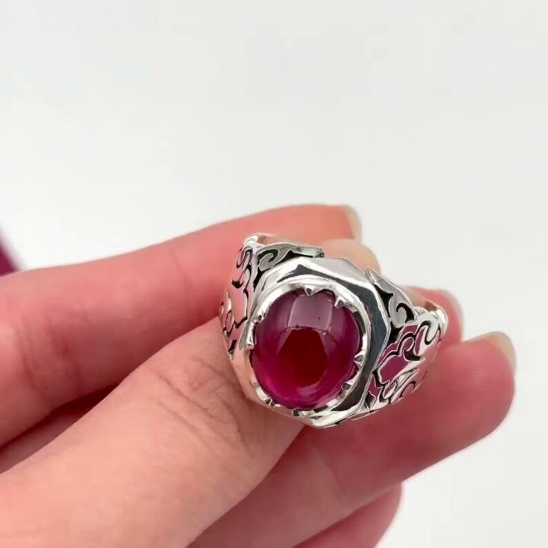 May include: A silver ring with an ornate design and a large, oval-shaped ruby gemstone.
