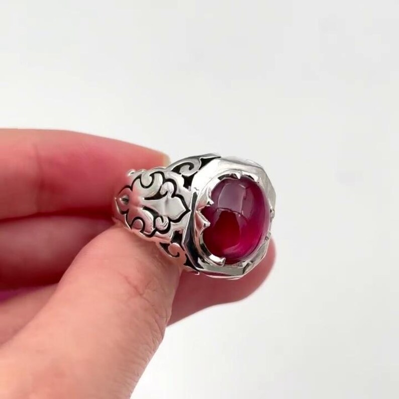 May include: A silver ring with an ornate design and a large, oval-shaped, red gemstone.