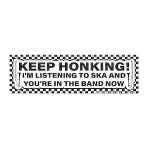 Könnte beinhalten: Rechteckiger Aufkleber mit schwarz-weiß kariertem Rand. Der Text lautet "KEEP HONKING! I'M LISTENING TO SKA AND YOU'RE IN THE BAND NOW" in fetten weißen Buchstaben. Posaunen-Illustrationen flankieren den Text.