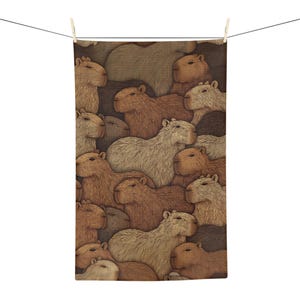 May include: A rectangular kitchen towel featuring a repeating pattern of capybaras in various shades of brown, tan, and beige. The illustration shows multiple capybaras overlapping in a dense, textured arrangement, hanging from a thin black line.
