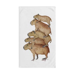 May include: A white towel featuring a watercolor illustration of five capybaras stacked on top of each other. The capybaras are various shades of brown and tan, with detailed fur textures. The towel is rectangular.