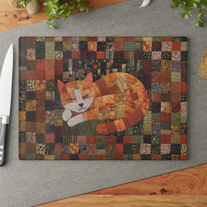 May include: A rectangular glass cutting board featuring a patchwork design of small squares in shades of orange, brown, green, and black. The center displays a sleeping cat composed of various fabric-like patterns in warm autumn tones.
