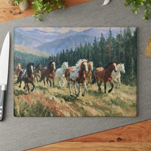 May include: A rectangular glass cutting board featuring a printed painting of a herd of horses running through a grassy field. The scene includes brown, white, and black horses with a backdrop of dense pine trees and distant blue mountains.