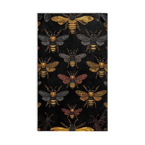 Puede incluir: Una manta rectangular negra con un patrón repetido de ilustraciones detalladas de abejas en oro, marrón y rojo. Las abejas tienen intrincados diseños de alas y cuerpo. La manta está hecha de un material suave.