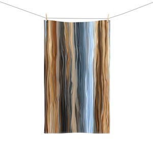 May include: A rectangular towel with a vertical striped pattern in shades of brown, tan, gray, and blue is hanging from a clothesline. The towel is held in place by two wooden clothespins against a white background.