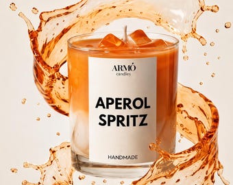 May include: A clear glass candle with orange wax and a white label reading ARMÓ candles APEROL SPRITZ HANDMADE. The candle contains wax cubes resembling ice and is surrounded by a dynamic, circular splash of orange liquid with droplets.
