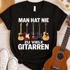 Può includere: Una t-shirt nera a maniche corte con il testo bianco MAN HAT NIE ZU VIELE GITARREN e una grafica di cinque diverse chitarre elettriche e acustiche nei toni del giallo, rosso, rosso scuro, nero e legno naturale al centro del petto.
