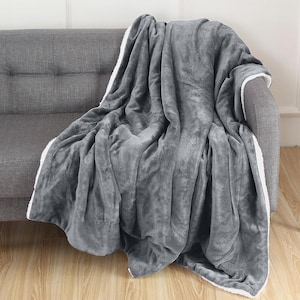 Puede incluir: Una manta de forro polar gris con ribete de sherpa blanco. La manta está colocada sobre un sofá gris.