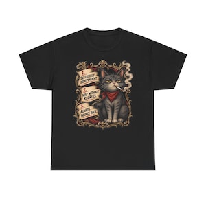 May include: A black t-shirt featuring a graphic of a grey cat wearing a red bandana with a cigarette in its mouth. The cat is framed by an ornate gold border and three numbered text banners that read: 1. BE FIERCELY INDEPENDENT. 2. NAP WITHOUT REGRETS. 3. ALWAYS BOUNCE BACK.