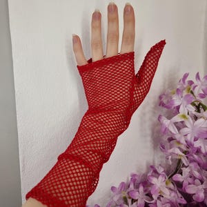 Puede incluir: Guantes de red rojos con un diseño largo sin dedos. Los guantes están hechos de un material elástico y ligero y tienen un delicado ribete de encaje.