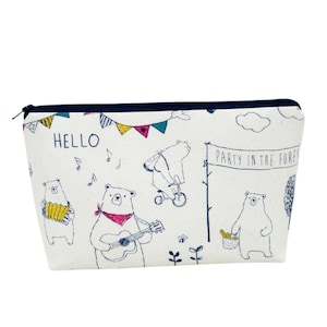 May include: A white canvas cosmetic bag with a black zipper and navy blue trim. The bag features a whimsical illustration of bears playing musical instruments and riding a bicycle. Text includes "HELLO" and "PARTY IN THE FOREST".