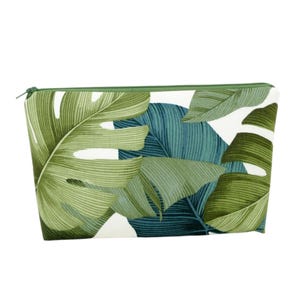 May include: A white zippered pouch with a tropical leaf print in shades of green and blue.
