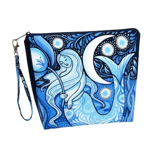 May include: A blue zippered pouch with a wrist strap, featuring a mermaid illustration. The design includes a mermaid holding a flower, a crescent moon, and floral and aquatic elements in shades of blue and white.