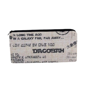 May include: A rectangular pencil case with a black zipper. The case is beige with black text that reads "A LONG TIME AGO IN A GALAXY FAR, FAR AWAY..." and "DAGOBAH". The case has a black border.