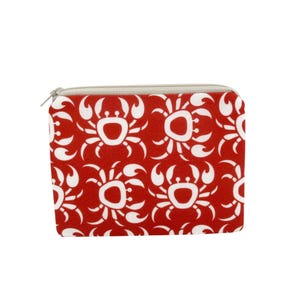 May include: A red zippered pouch with a repeating white crab pattern. The pouch has a silver zipper and a rectangular shape. The crab design is a stylized, symmetrical pattern.
