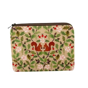 May include: A rectangular zippered pouch featuring a tan background with a repeating pattern of brown squirrels, green oak leaves, acorns, and small pink flowers. The pouch has a dark brown zipper closure along the top edge of the rectangular structure.