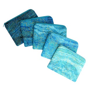 May include: A collection of six zippered pouches in varying shades of blue and turquoise. Each pouch features a unique pattern with gold accents. The pouches are arranged diagonally, showcasing their individual designs and textures.