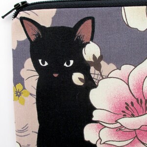 May include: A black cat with white flowers printed on a gray fabric pouch. The pouch has a zipper closure.