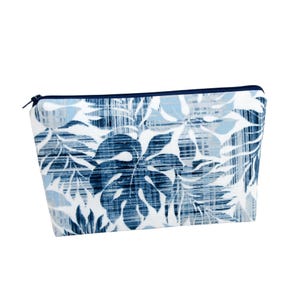 May include: A rectangular cosmetic bag with a tropical leaf pattern in shades of blue and white. The bag has a navy blue zipper and trim. The design features large, stylized leaves and smaller foliage, creating a botanical theme.