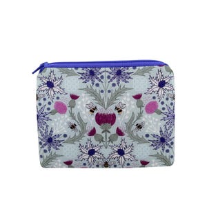 May include: A rectangular cosmetic bag with a blue zipper. The bag features a repeating pattern of purple thistles, gray leaves, and bees on a light blue background. The bag is designed for storing makeup and other beauty products.