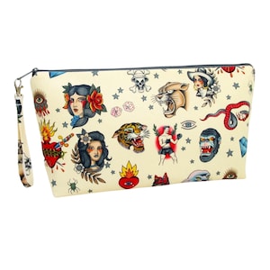 May include: A cream-colored zippered pouch with a colorful tattoo-inspired print. The print features images of a tiger, panther, snake, heart, skull, and other traditional tattoo designs.