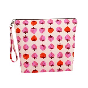 May include: A cream-colored zippered pouch with a wrist strap, patterned with repeating pink and red strawberries. The strawberries have green stems and are arranged in a grid pattern. The zipper is black, and the wrist strap is the same cream color as the pouch.