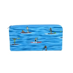 May include: A rectangular blue pencil case featuring a repeating pattern of people paddleboarding on water. The design includes various figures on stand-up paddleboards with paddles, some accompanied by a dog, set against a wavy blue background.