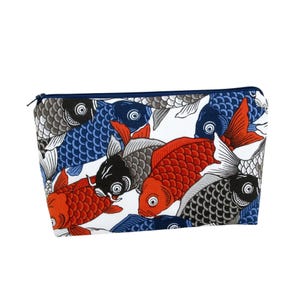 May include: A rectangular cosmetic bag with a zipper closure. The bag features a repeating pattern of koi fish in red, black, blue, and gray against a white background. The zipper is navy blue.
