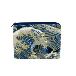 May include: A rectangular pouch with a navy blue zipper and a Japanese wave pattern. The design features stylized waves in shades of blue and gold, creating a textured, artistic look. The pouch is likely made of fabric.