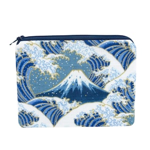 May include: A rectangular, zippered pouch featuring a Japanese-inspired design. The pouch showcases a blue and white wave pattern with a central image of Mount Fuji. The mountain is depicted with a snow-capped peak. The zipper is navy blue.