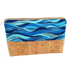 May include: A blue and gold fabric zippered pouch with a cork bottom. The fabric features a wavy pattern.
