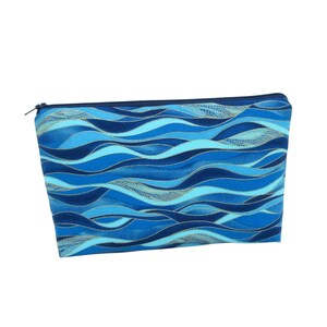 May include: A rectangular zippered pouch with a blue wave pattern. The pouch features shades of blue, from light to dark, with gold accents. The zipper is dark blue, and the pouch appears to be made of fabric.