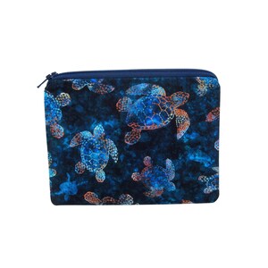May include: A rectangular, zippered pouch featuring a repeating pattern of blue and orange sea turtles on a dark blue background. The pouch has a navy blue zipper and trim, and is likely made of fabric.