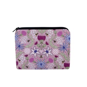 May include: A rectangular lavender zippered pouch with a floral pattern featuring purple thistles, blue flowers, green leaves, and bees. The pouch has a black zipper and a black zipper pull.