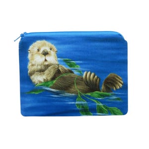 May include: A blue zippered pouch with a printed image of a sea otter floating on its back in the water with kelp. The otter is brown and has a white chest.