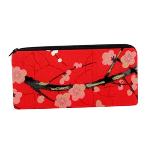 May include: A rectangular red pencil case with a black zipper. The case features a floral design with pink blossoms, black branches, and gold accents. The design is reminiscent of Japanese art.