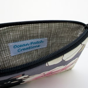 May include: A gray zippered pouch with a floral print and a brown fabric lining. The pouch has a label that reads "Ocean Patch Creations".