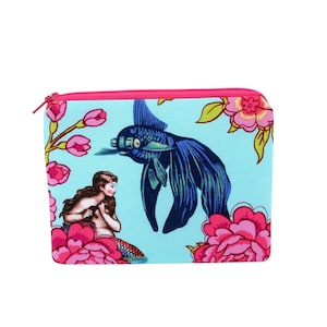 May include: A small, rectangular zippered pouch with a light blue background. The pouch features a dark blue fish and a mermaid surrounded by pink flowers. The zipper is pink.