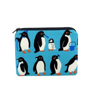 May include: A rectangular, zippered pouch with a light blue background. The pouch is decorated with a pattern of cartoon penguins in various poses, with black and white bodies, orange feet, and some with accessories.