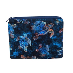 May include: A rectangular zippered pouch featuring a pattern of blue and orange sea turtles against a dark blue background. The turtles have detailed shell patterns. The zipper is navy blue.
