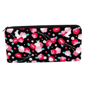 May include: A black pencil case with a zipper closure, adorned with a floral pattern of pink and red blossoms, white rabbits, and small white stars. The design is set against a black background.