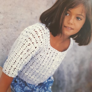 Peut inclure: Une jeune fille portant un haut en crochet blanc avec une jupe à motifs bleus et blancs.