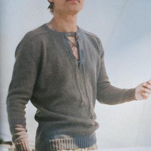 May include: A brown knitted sweater with a V-neck and a knotted detail at the neckline.